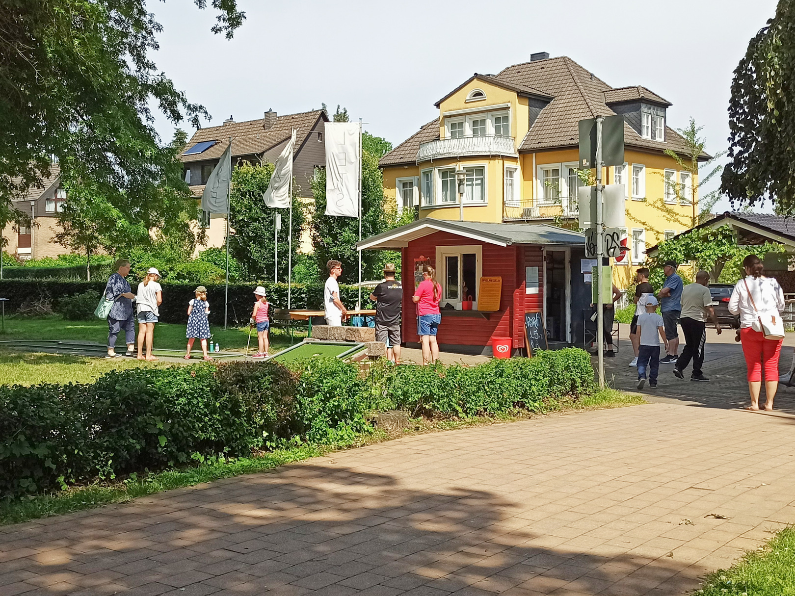 Menschen auf dem Minigolfplatz vor dem Kiosk